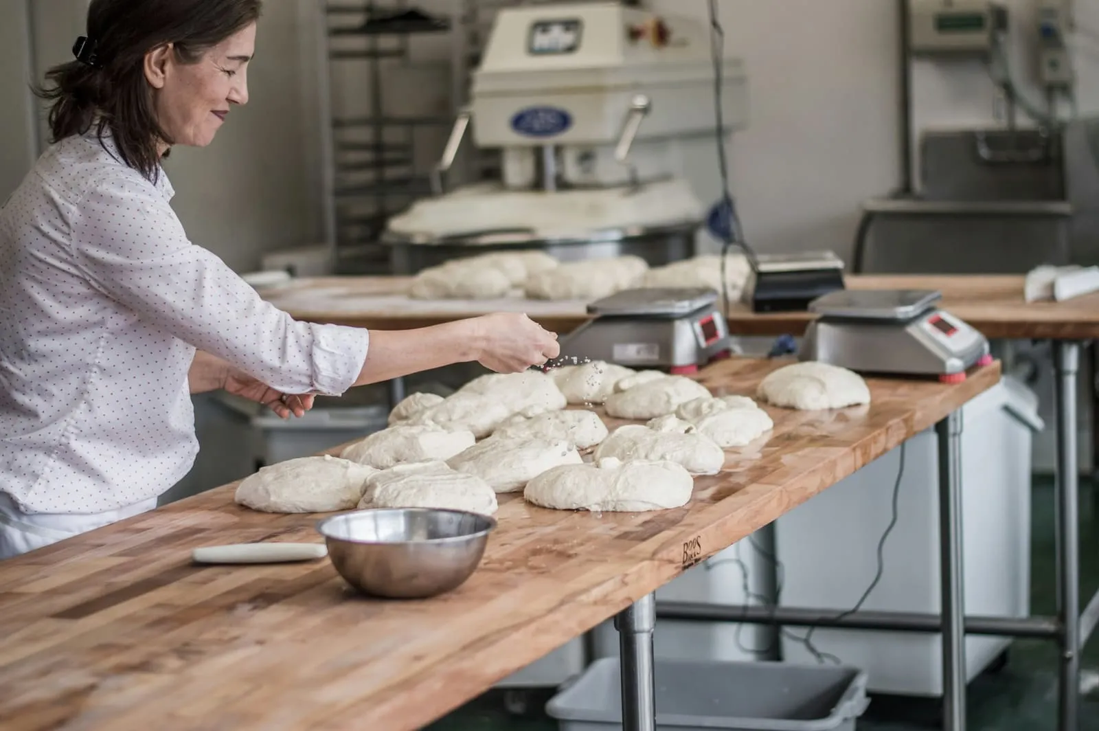 A baker shaping loaves on a floured bench