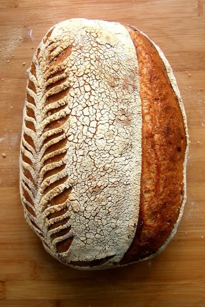A scored sourdough loaf on a wooden board